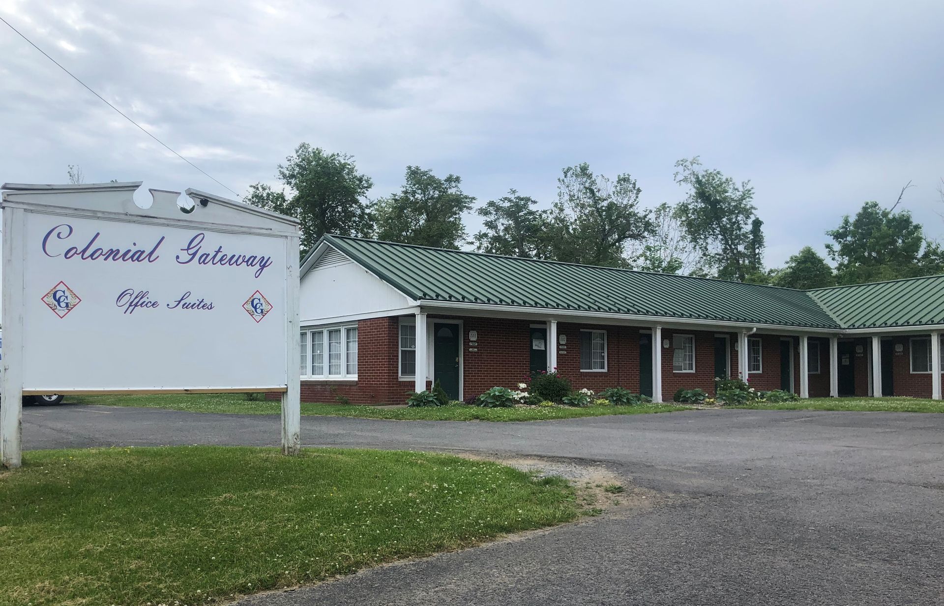Sign for Colonial Innway motel in front of a single-story brick building with a green tiled roof, on a cloudy day.