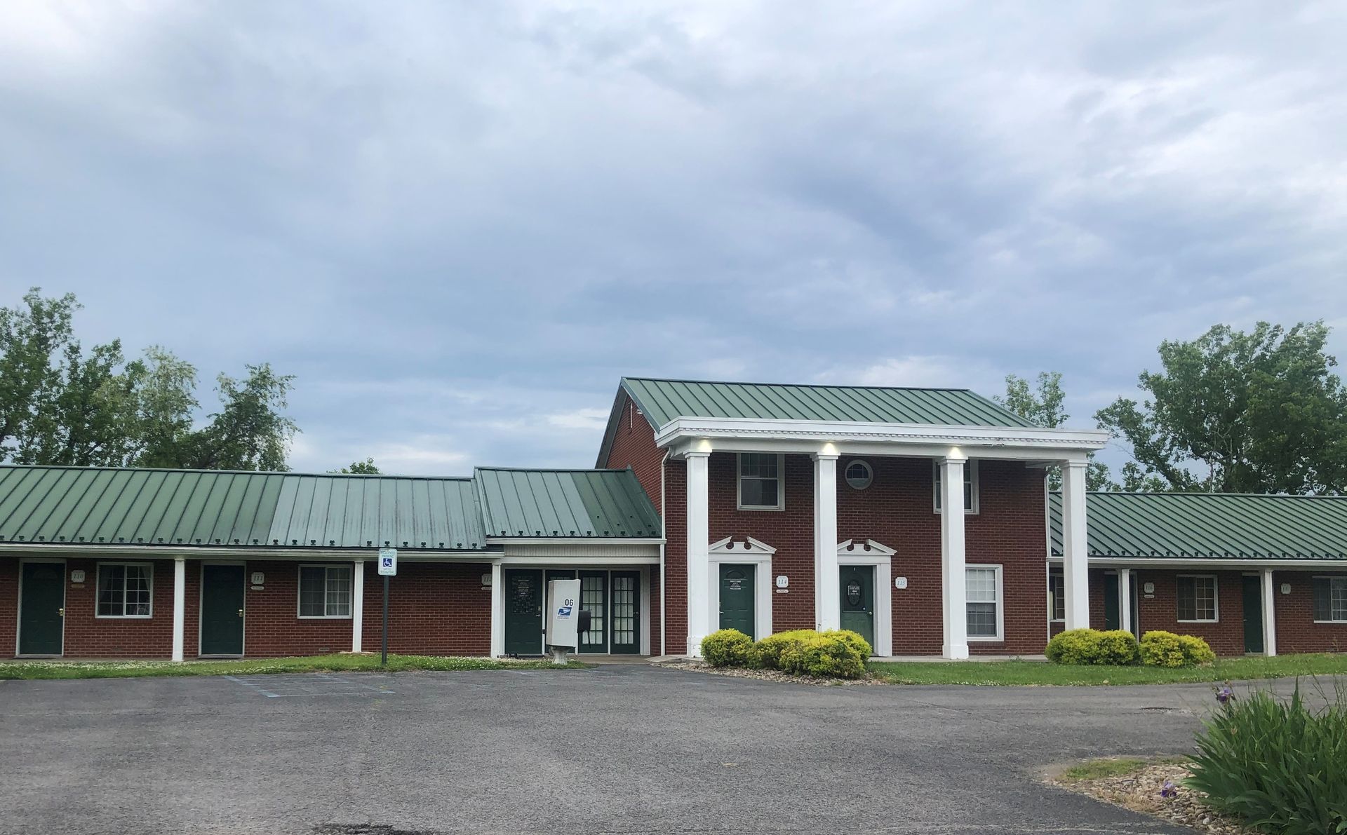 A brick motel with a green roof and white columns. The sky is overcast.