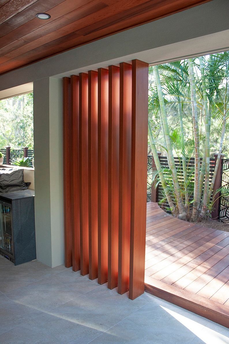 A series of vertical, reddish-brown wooden slats acting as a room divider next to a wooden deck outdoors. — Michael Duncan Constructions Pty Ltd in Robina, QLD