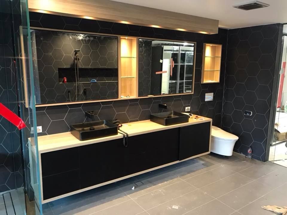 Modern bathroom with black hexagonal wall tiles, a wood vanity featuring two black sinks, and a large mirror with lighting. — Michael Duncan Constructions Pty Ltd in Burleigh Heads, QLD