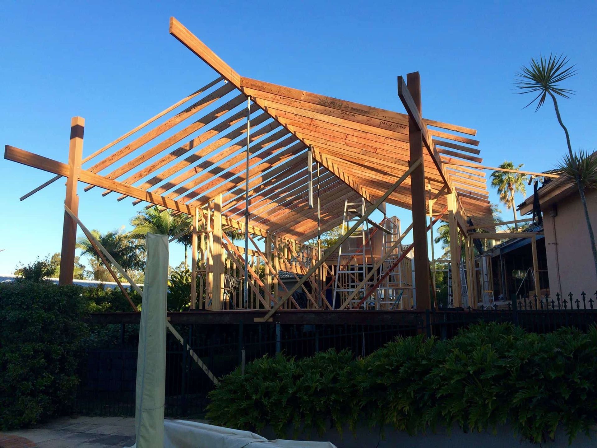 A wooden framework for a roof structure under construction, featuring exposed beams set against a clear blue sky. — Michael Duncan Constructions Pty Ltd in Robina, QLD