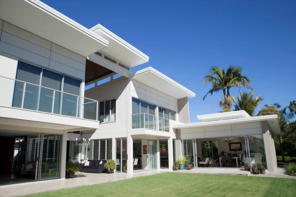 A modern two-story home with white walls, expansive glass windows, balconies, and an open patio overlooking a grass lawn. — Michael Duncan Constructions Pty Ltd in Robina, QLD
