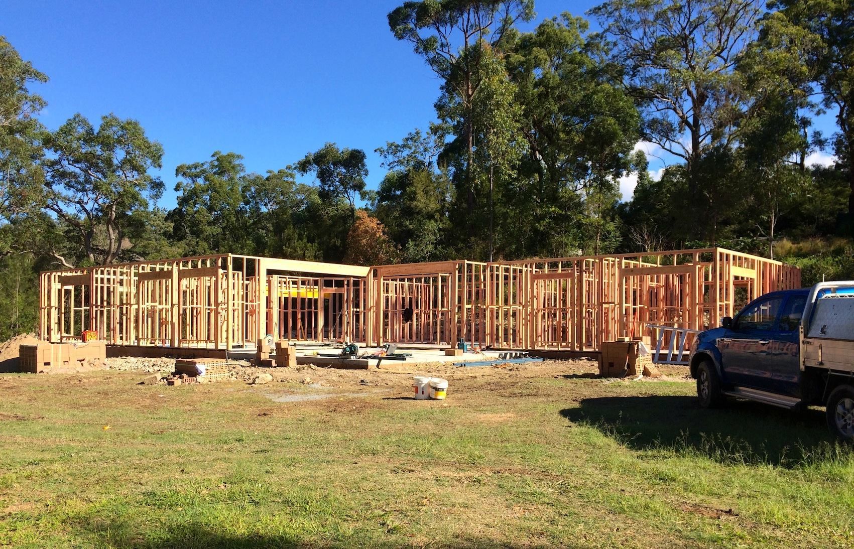 Wooden wall framing for a new house under construction on a sunny, grassy lot with trees in the background. — Michael Duncan Constructions Pty Ltd in Robina, QLD