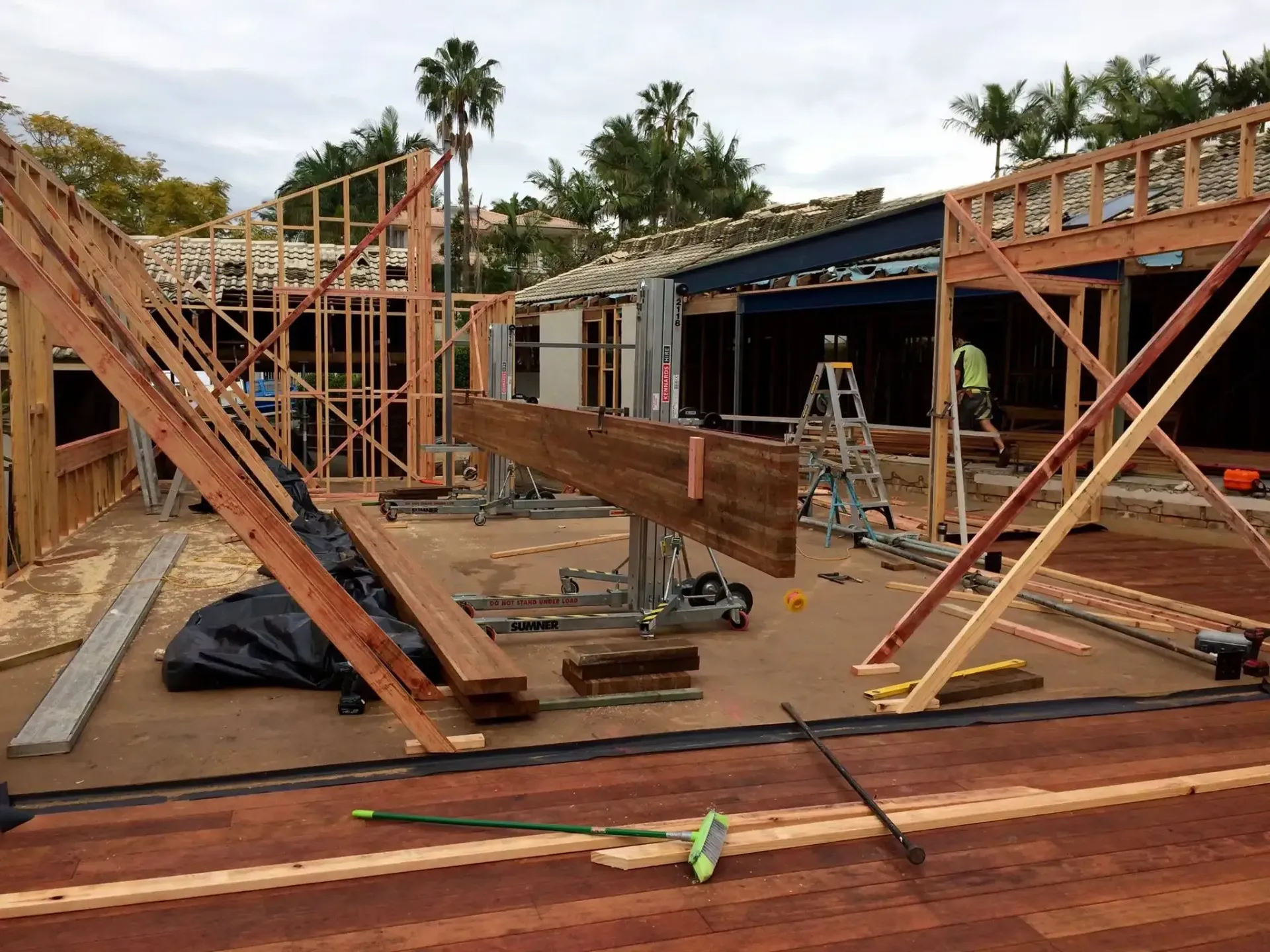 A construction site with wooden framing, a large horizontal beam supported by a metal lift, and a brick-paved foreground.— Michael Duncan Constructions Pty Ltd in Burleigh Heads, QLD