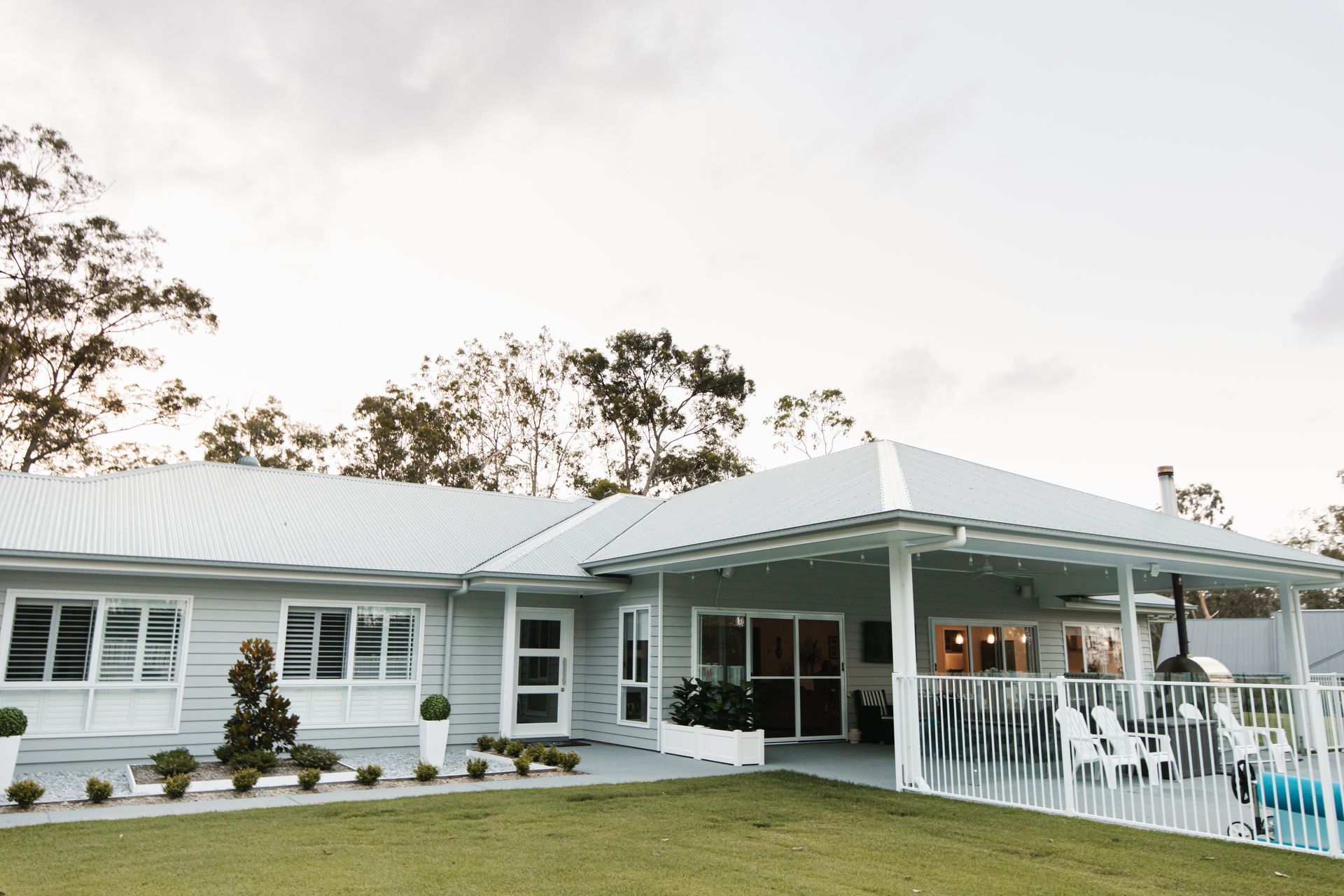 A light grey single-story suburban house with a white covered patio, swimming pool, and lawn against a cloudy sky — Michael Duncan Constructions Pty Ltd in Robina, QLD