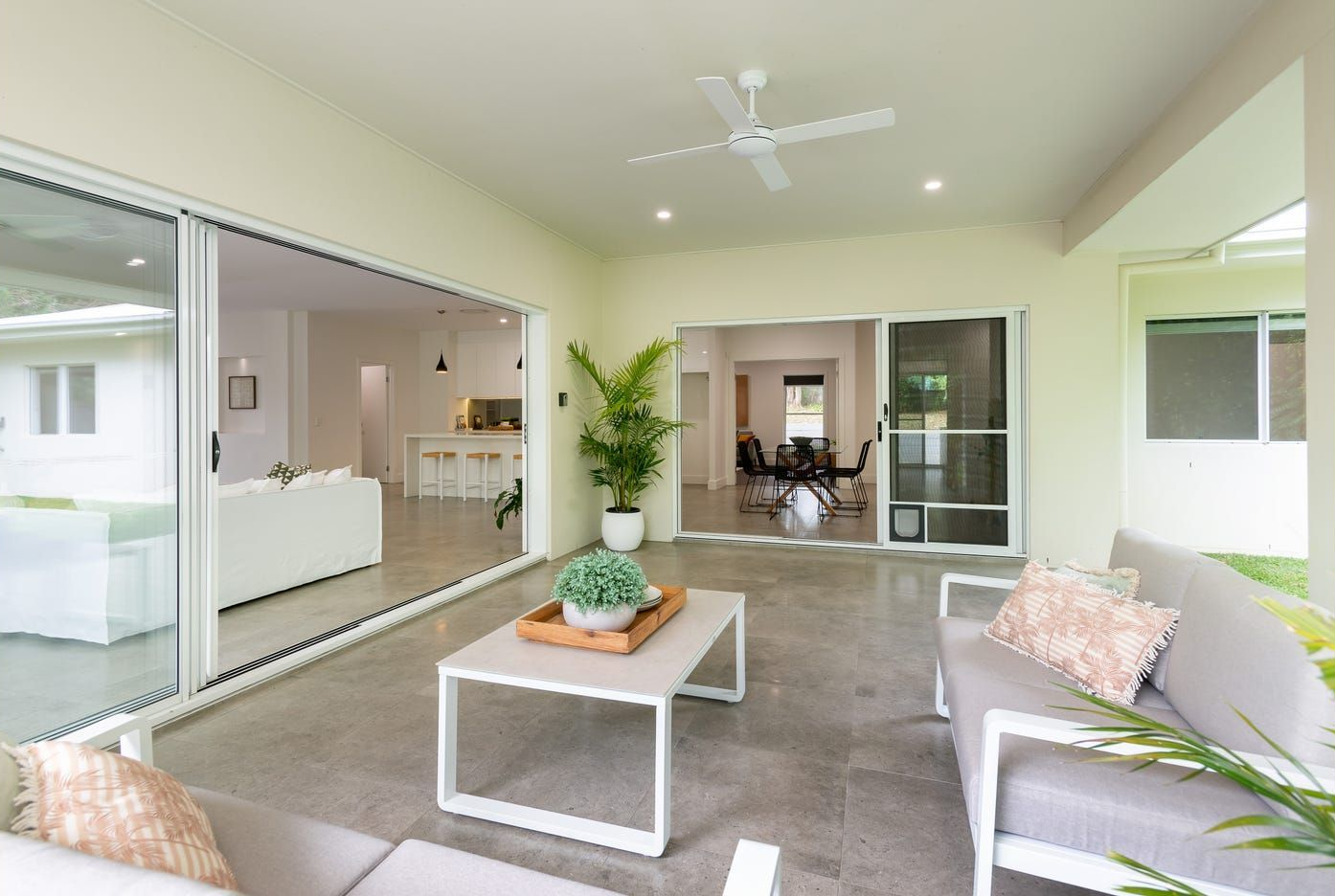 A bright, modern indoor-outdoor patio with sliding glass doors, neutral furnishings, a coffee table, and a ceiling fan. — Michael Duncan Constructions Pty Ltd in Ashmore, QLD