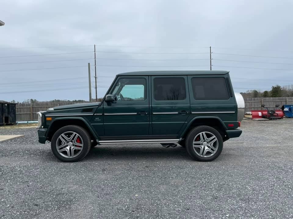 Dark green Mercedes-Benz G-Wagon SUV with silver accents, parked on gravel in a cloudy setting.