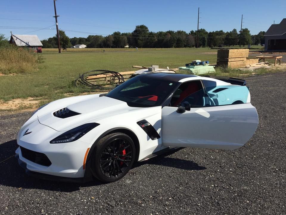 White Corvette with black accents and red brake calipers, door open, parked outdoors.