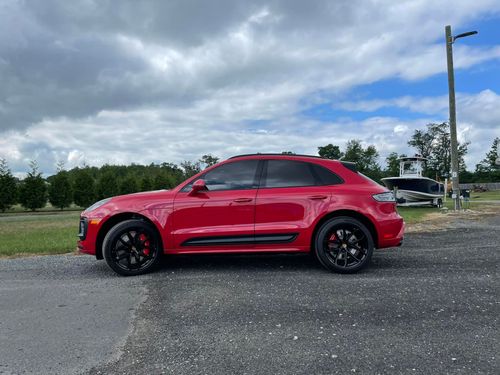 Red Porsche SUV parked on gravel with a cloudy sky backdrop. Red Porsche SUV parked on gravel with a cloudy sky backdrop.