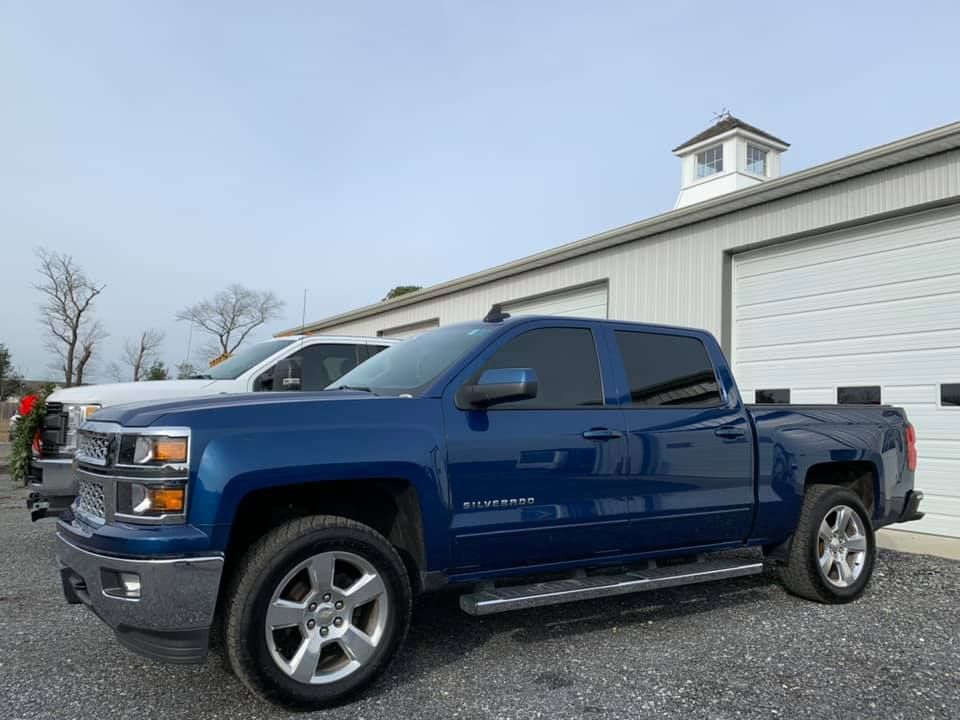 Blue Chevrolet Silverado pickup truck parked in front of a white building with garage doors.