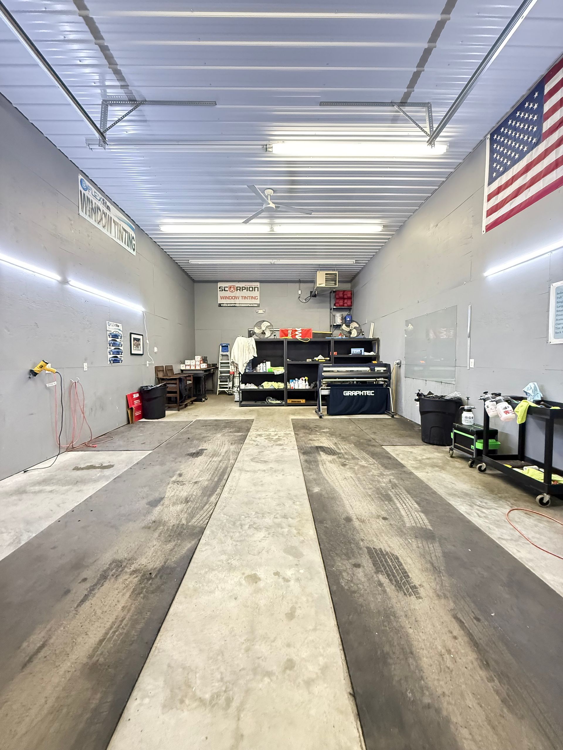 Inside a car wash bay, long concrete lanes lead to work area, flag on wall.