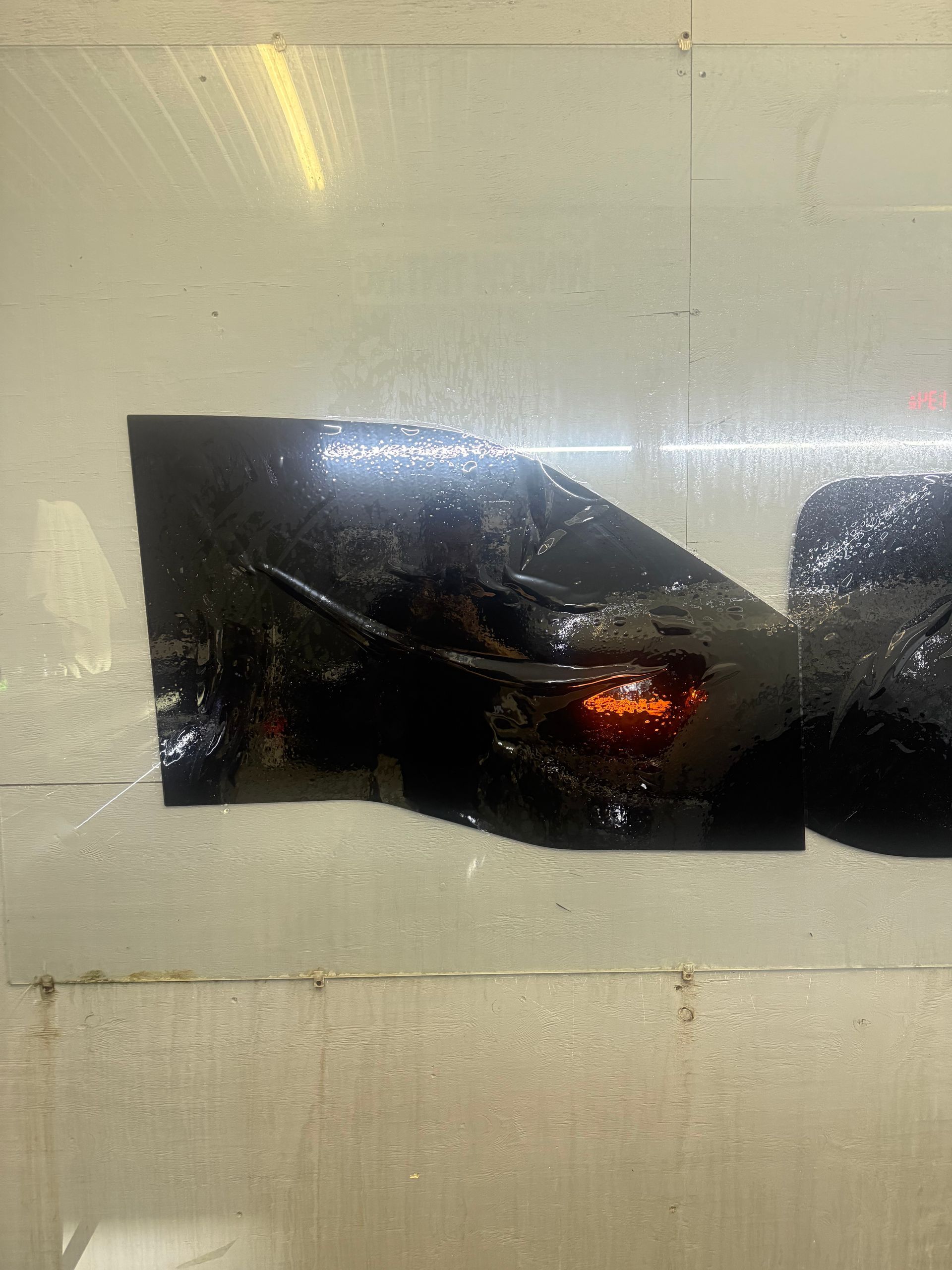 Black material with a reddish-orange glow against a metallic, shiny surface.