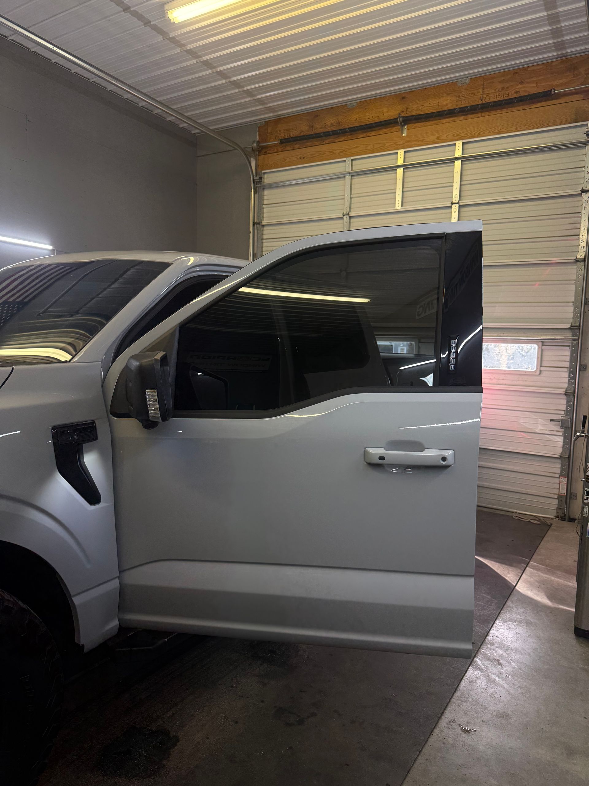 White Ford truck with tinted windows, parked inside a garage, door open.