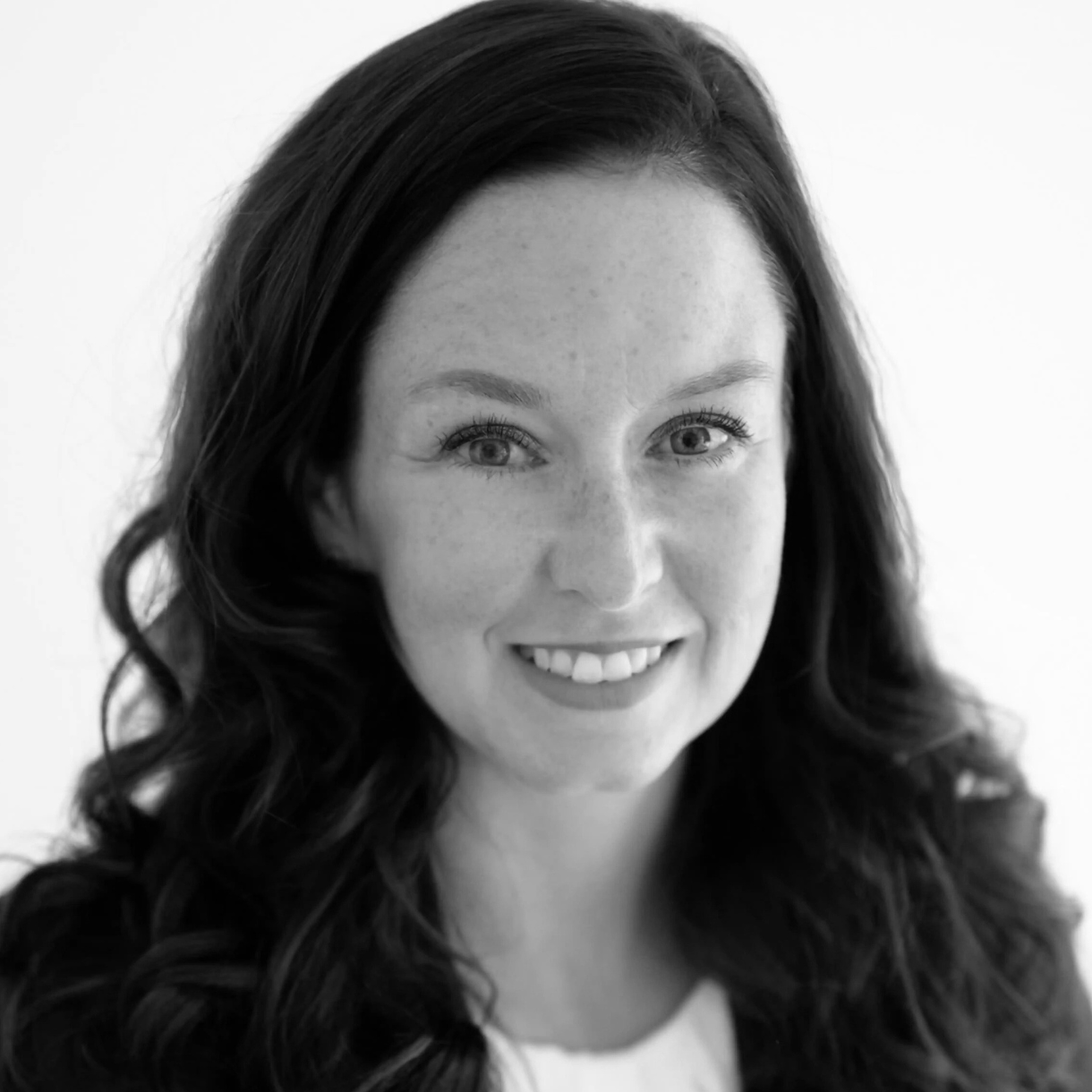 Woman with dark wavy hair smiles, looking at the camera.