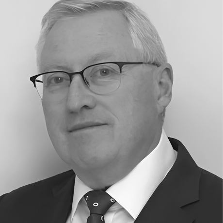 Man in glasses, suit, and tie, looking at the camera, headshot in grayscale.