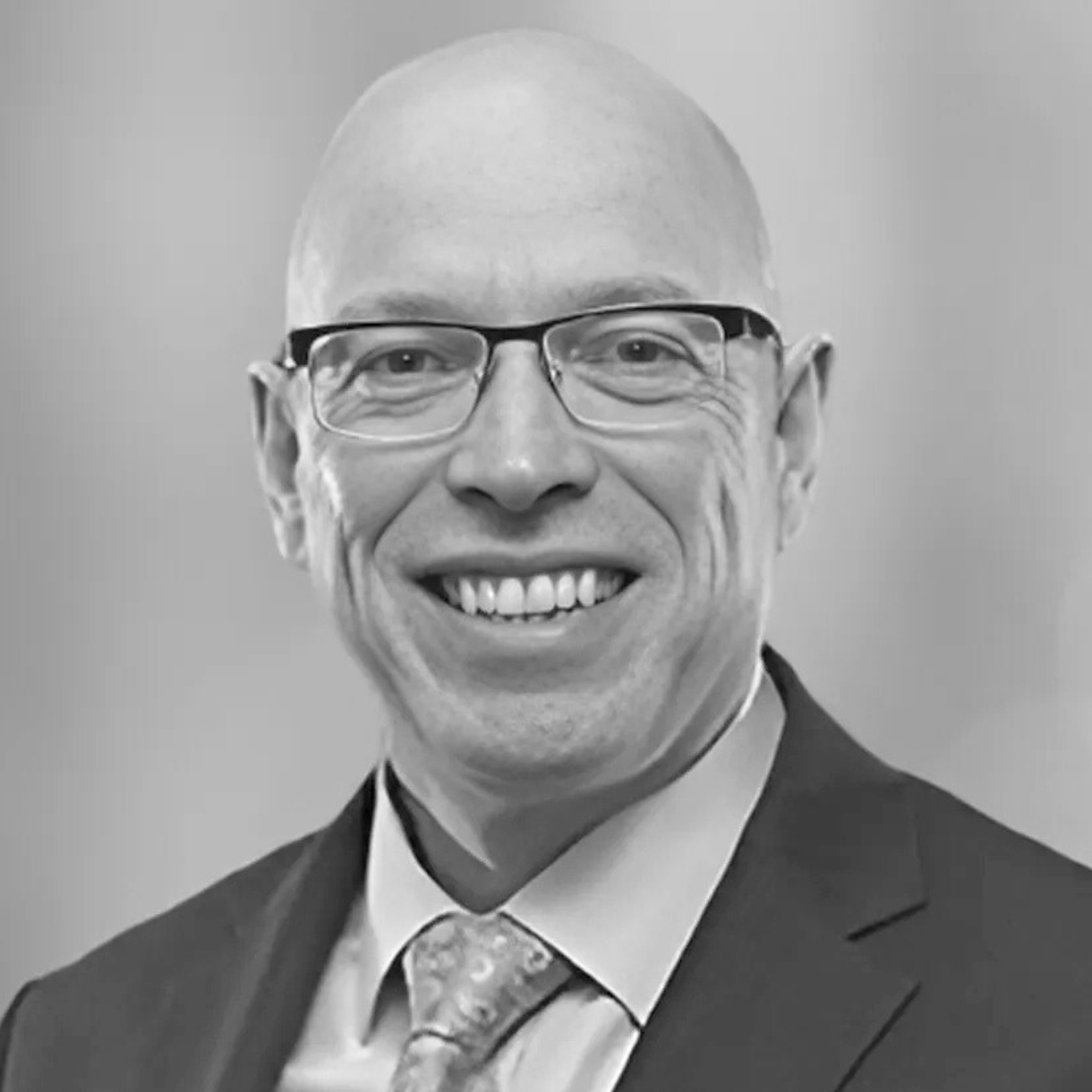Bald man wearing glasses, smiling, and wearing a suit and tie.