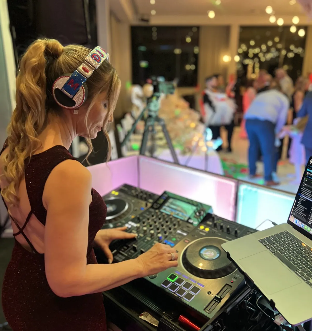 DJ with headphones, mixing music at an event, wearing a dark red dress.