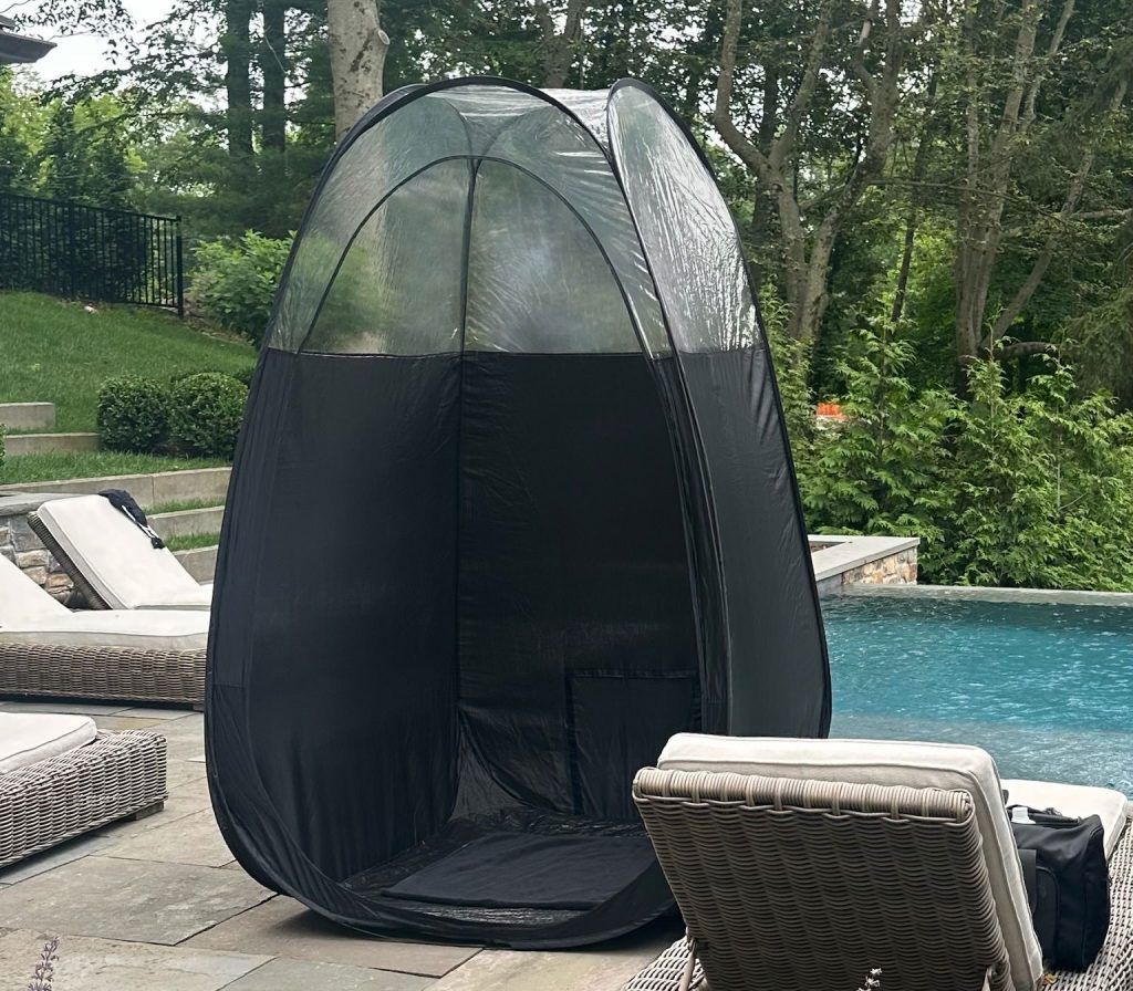 Black pop-up spray tan booth set up on a patio next to a swimming pool.