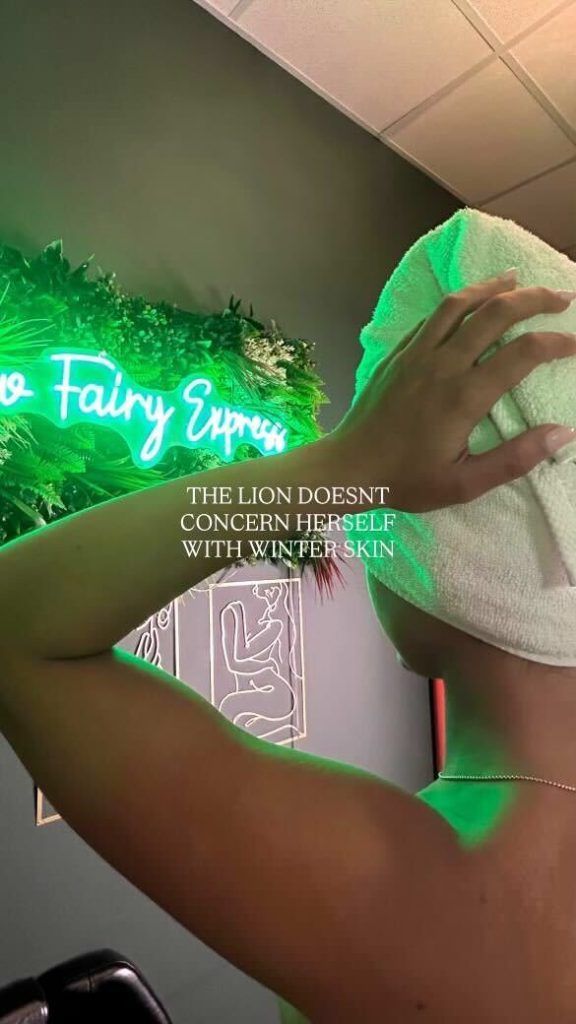 Woman with towel on head in front of neon sign, green light.