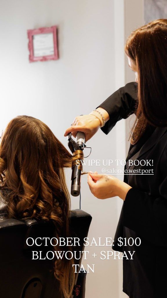 Stylist curling hair in a salon. October sale: $100 Blowout + Spray Tan.
