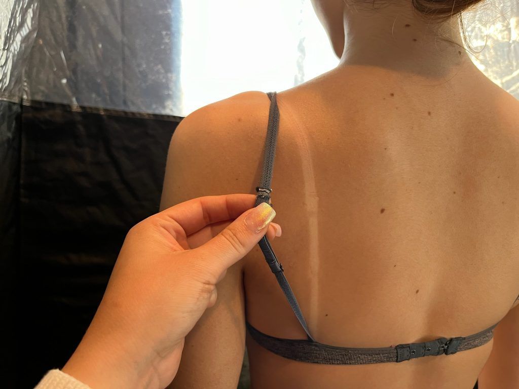Hand adjusting a thin strap on a person's bra, with their back to the camera.