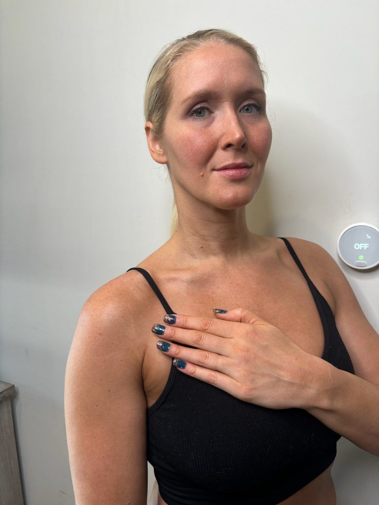 Woman in a black tank top, hand on chest, looking at the camera.