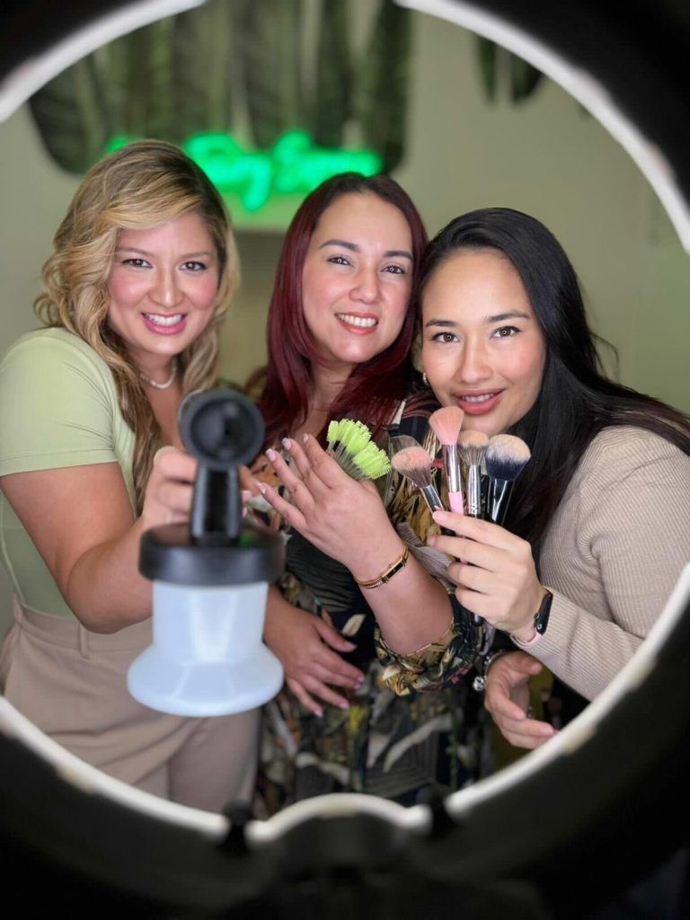 Three women holding beauty tools, lit by a ring light.