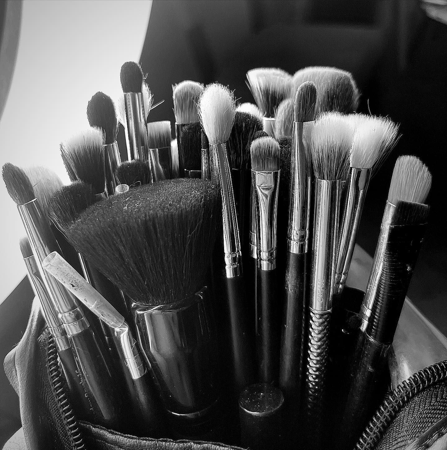 Black and white photo of a collection of makeup brushes in a cylindrical container.