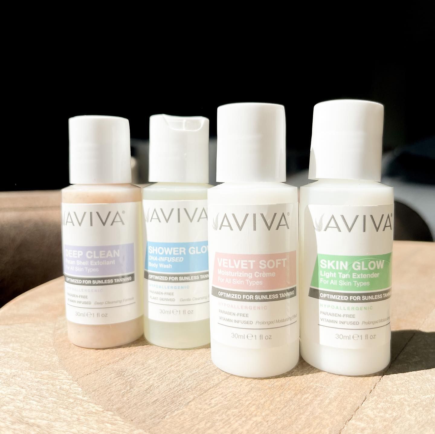 Four bottles of Aviva skincare products on wood. Each bottle is white with a different colored label.