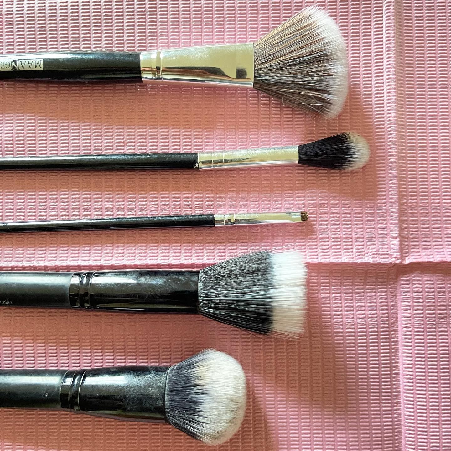 Makeup brushes with black handles and white bristles, laid on a pink textured surface.