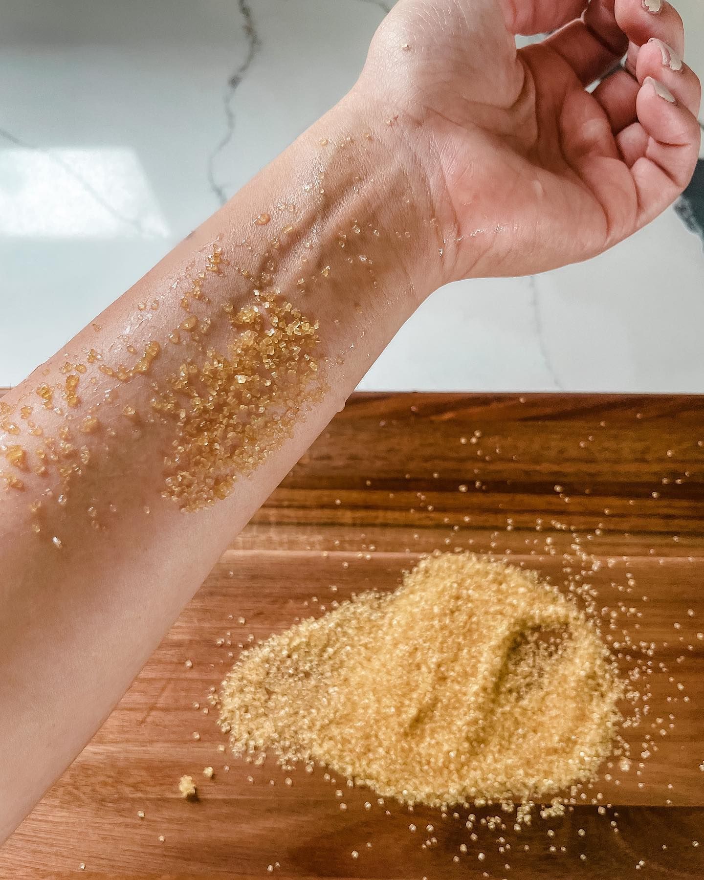Arm covered in brown sugar on a wooden board. Sugar scattered below the arm.