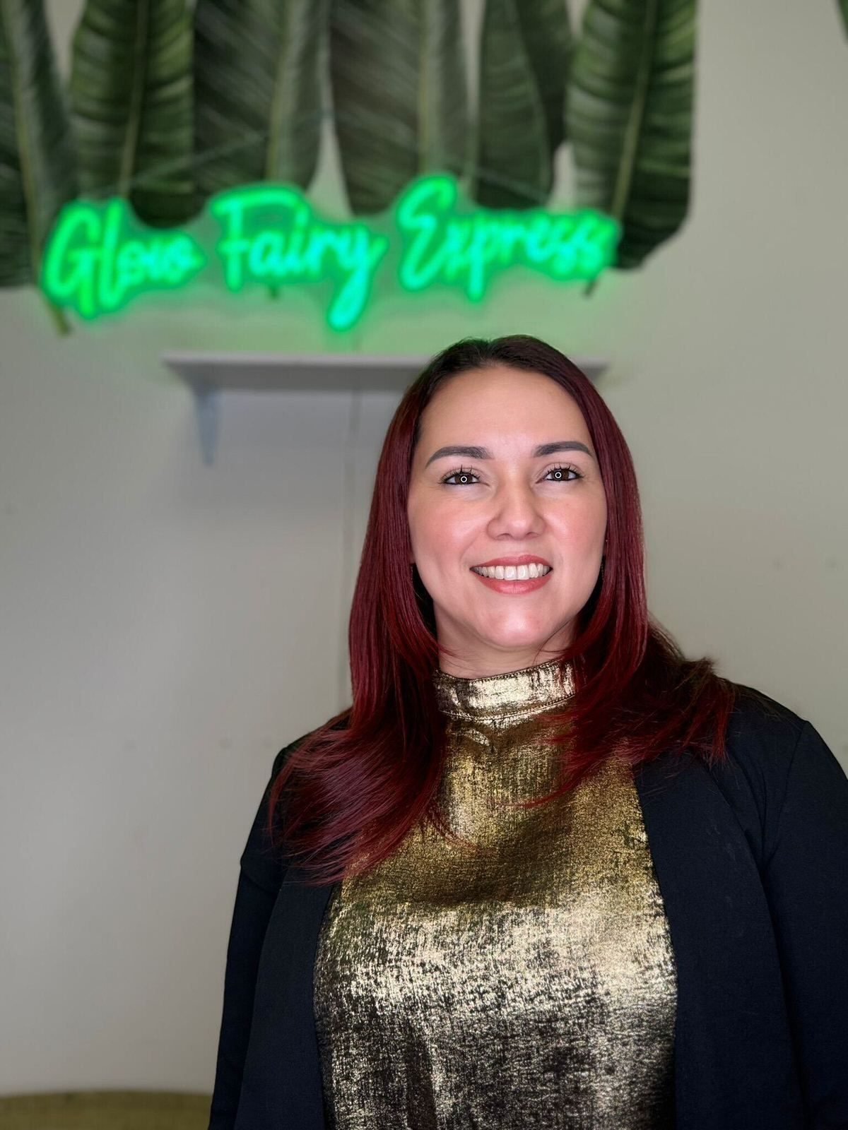 Woman with auburn hair smiles in front of a neon 