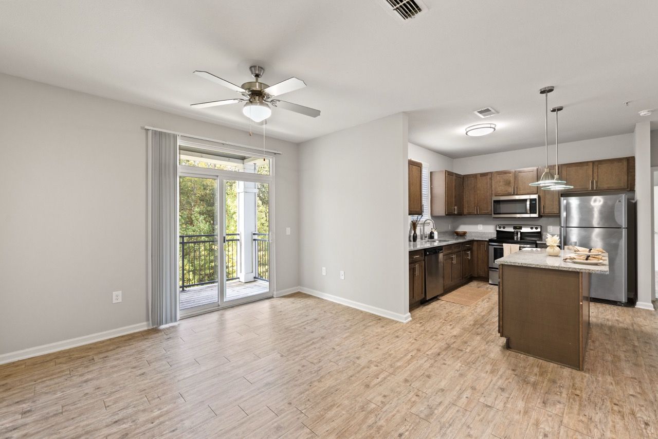 Open living area with kitchen, island, stainless-steel appliances, and sliding balcony door.