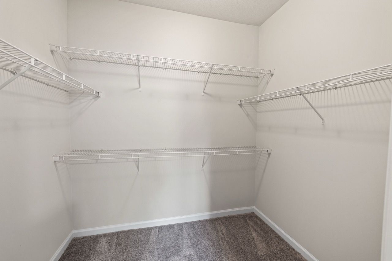 Empty walk-in closet with white wire shelving and beige walls.