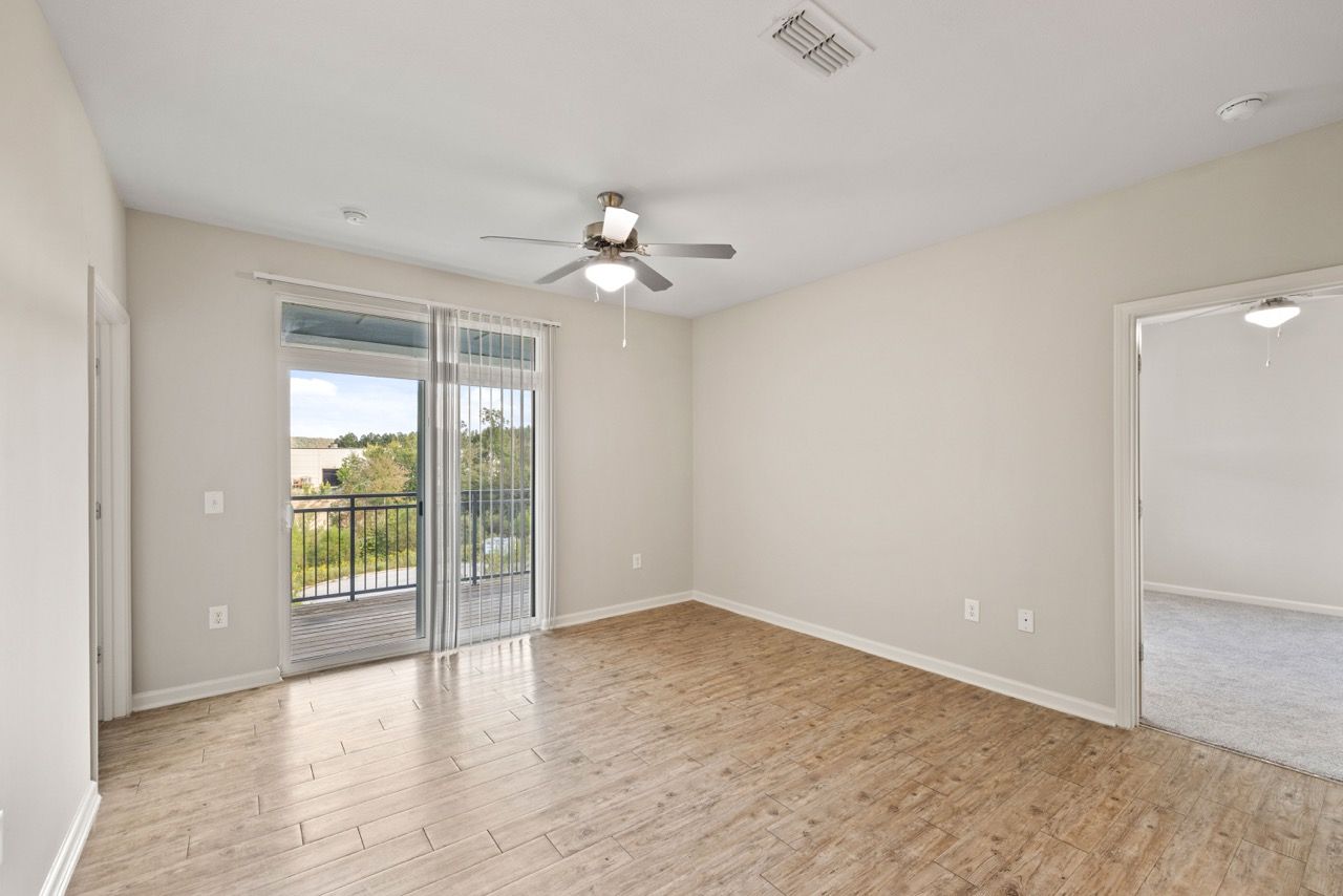 Living room with sliding glass door to balcony, ceiling fan, and wood-look flooring.