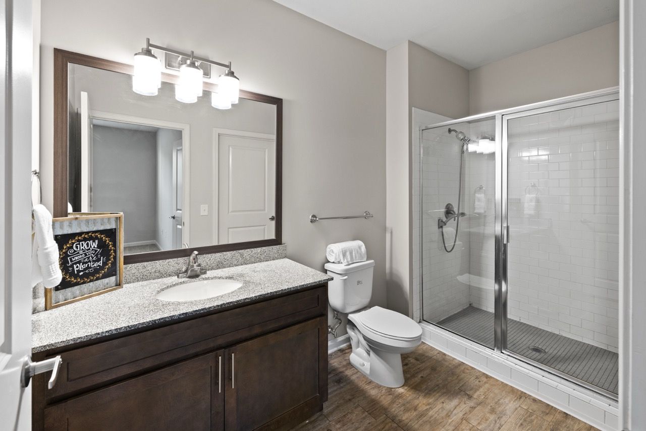 Bathroom with dark wood vanity, granite countertop, toilet, and glass-enclosed shower.