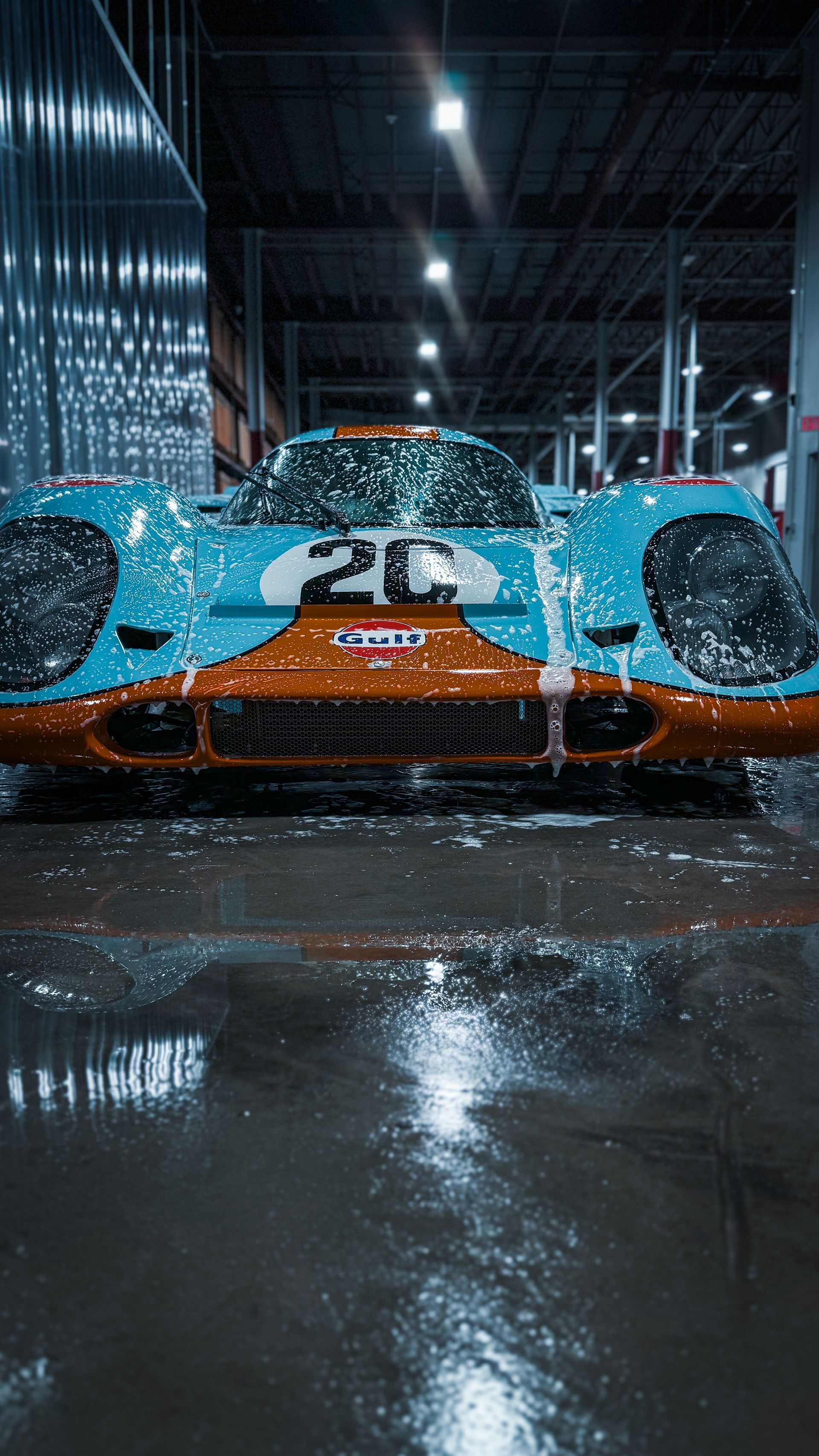 A blue and orange race car, being washed. Water and soap cover the car in a garage.