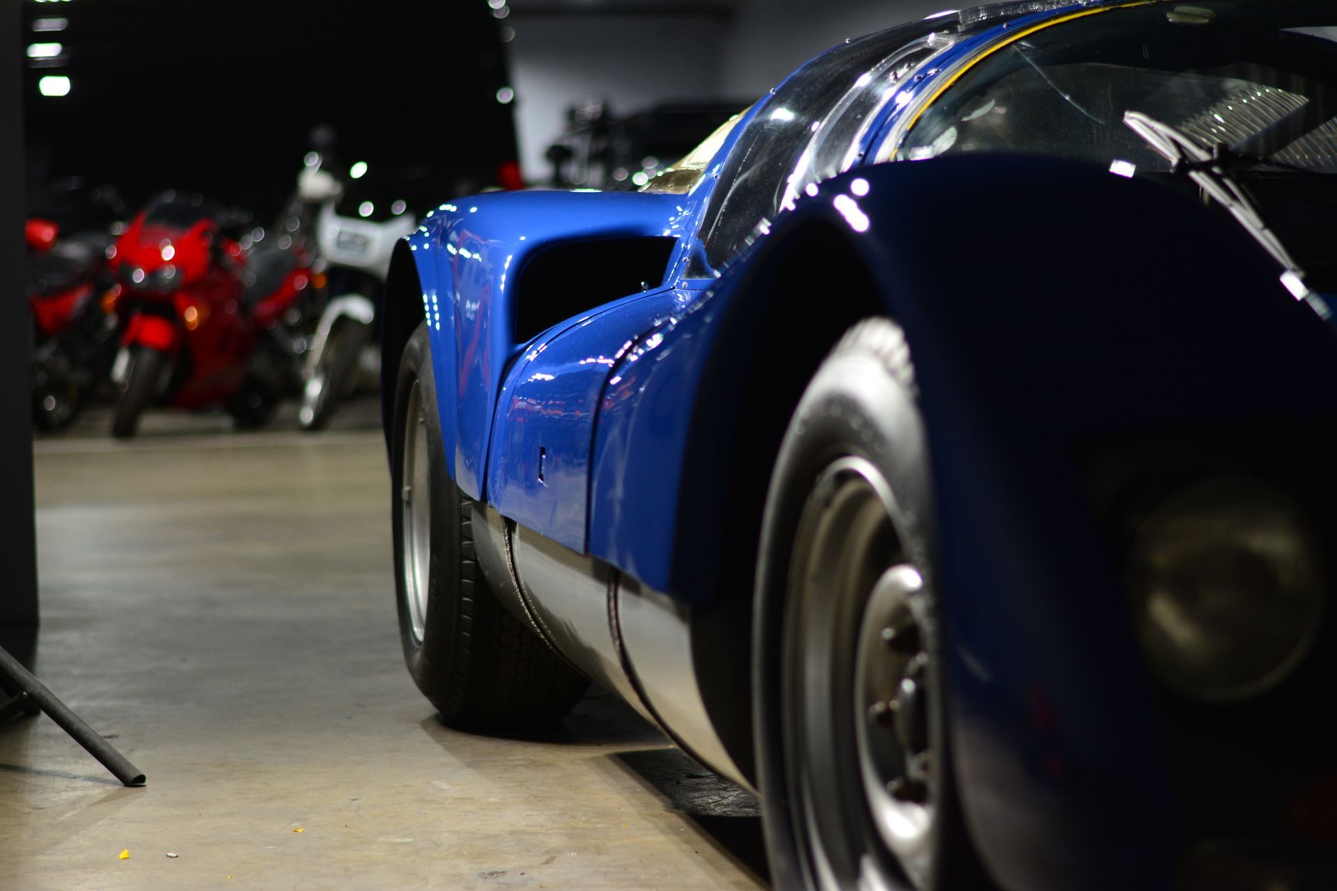 Blue sports car parked indoors with motorcycles in the background.