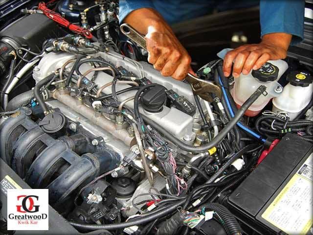 Mechanic working on a car engine with tools, hands visible.
