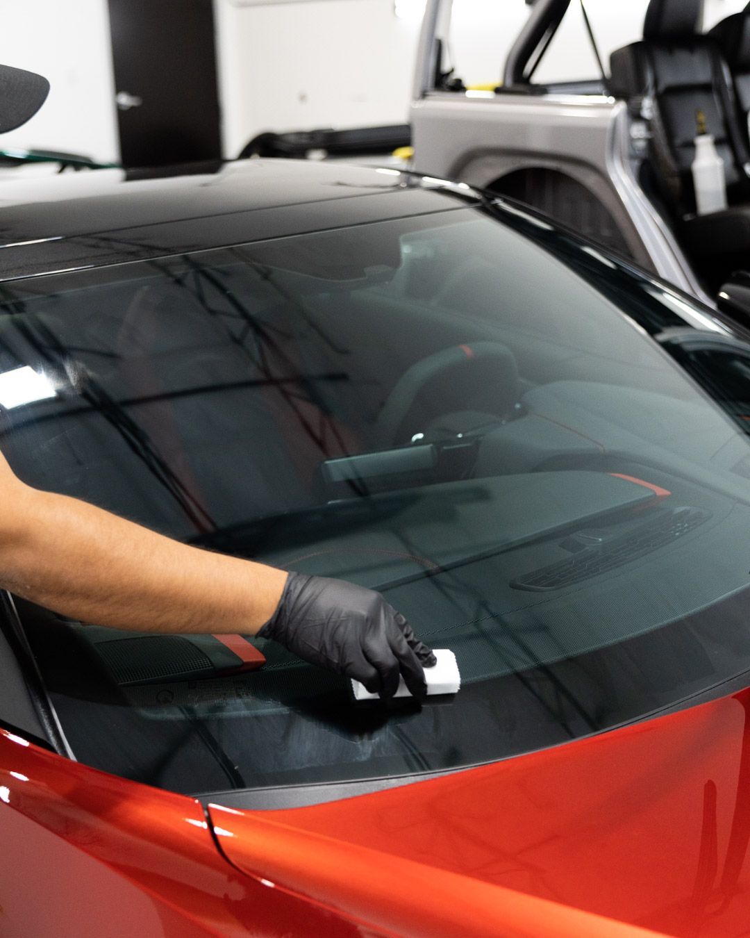 A man is cleaning the windshield of a red car.