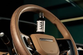 A bottle of lux is sitting on the steering wheel of a car.