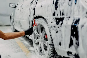 A man is washing a car with foam and a brush.