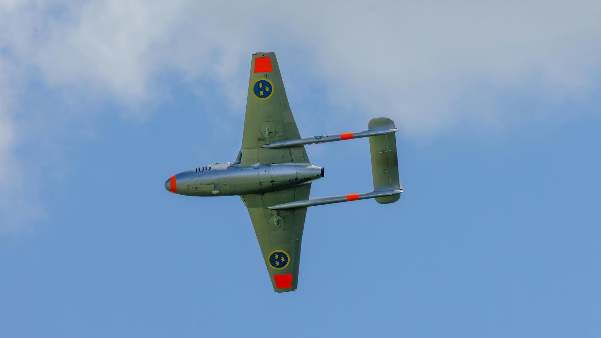 A small fighter jet is flying through a cloudy blue sky.
