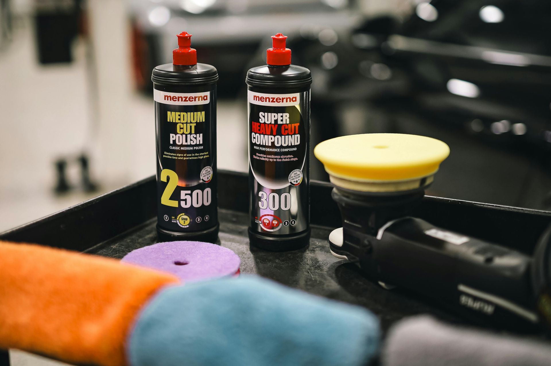 Two bottles of heavy cut polish are sitting on a tray next to a polisher.