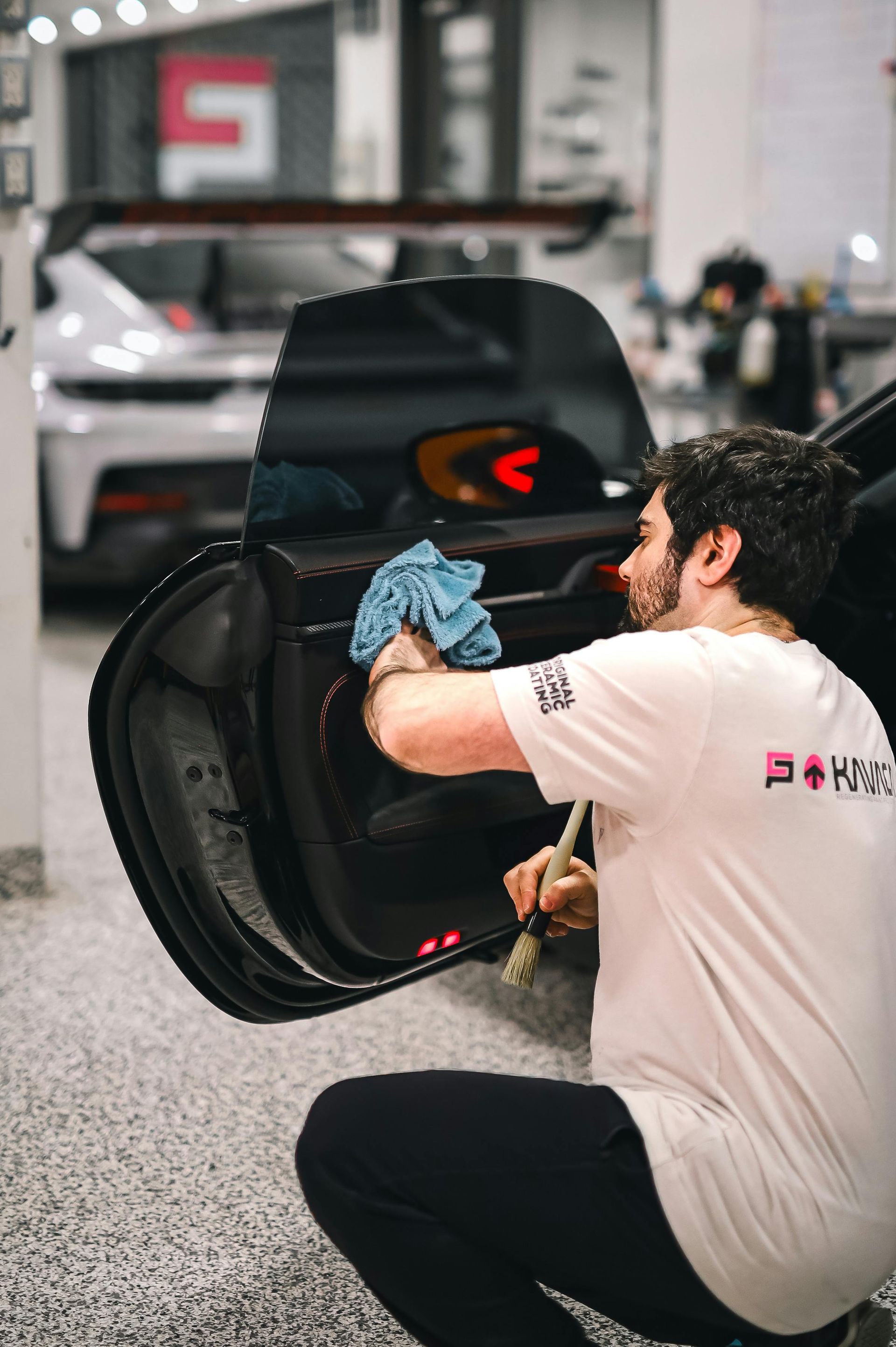 A man is cleaning the door of a car with a towel.