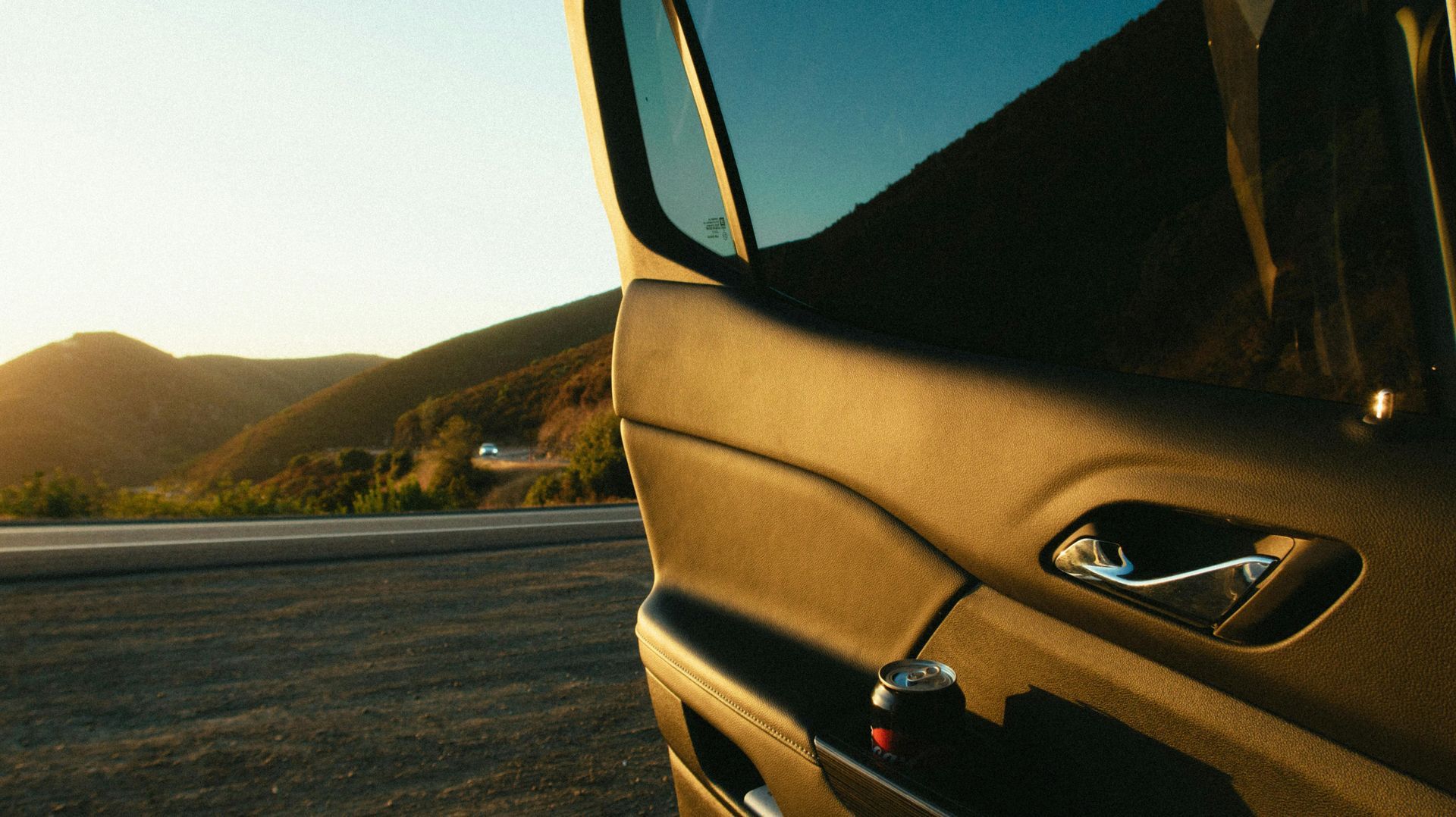 A car is parked on the side of the road with mountains in the background.