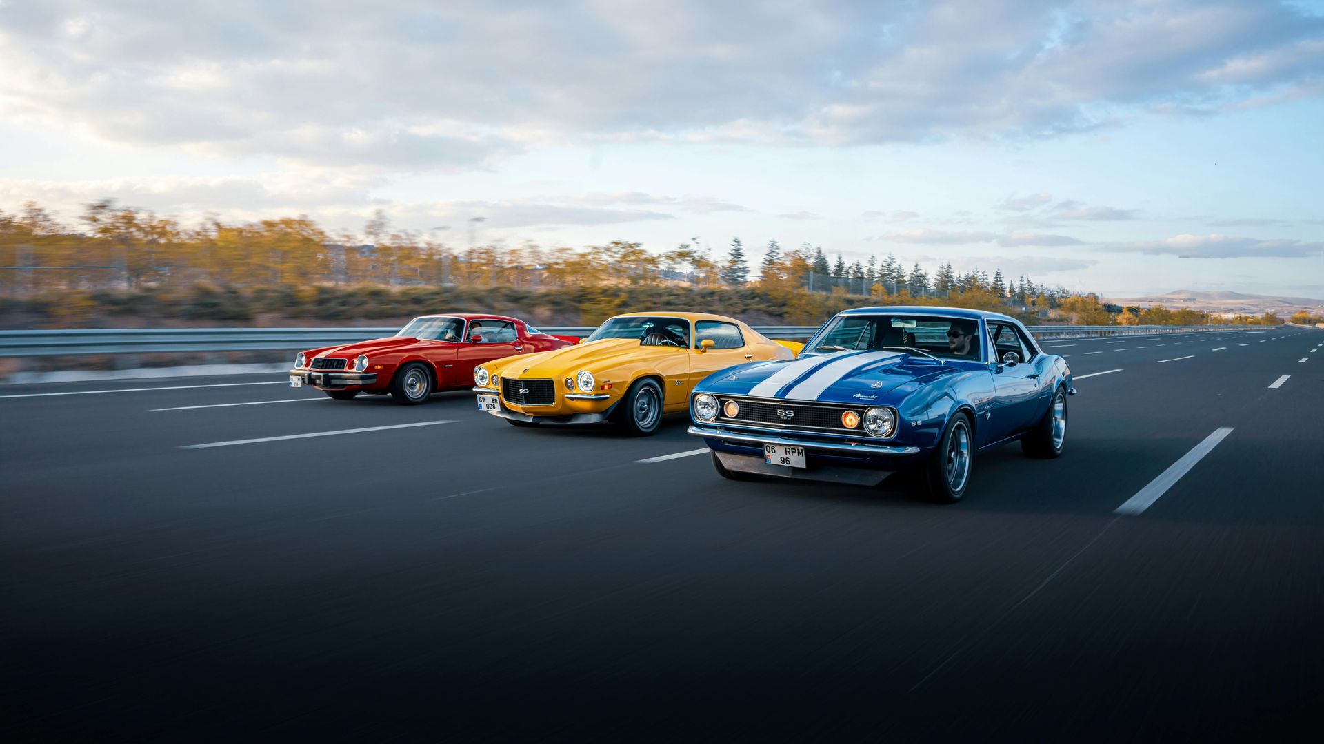 Three classic cars are driving down a highway.