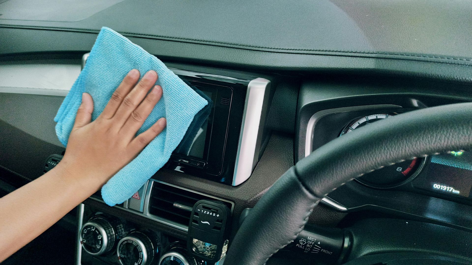 A person is cleaning the dashboard of a car with a blue cloth.