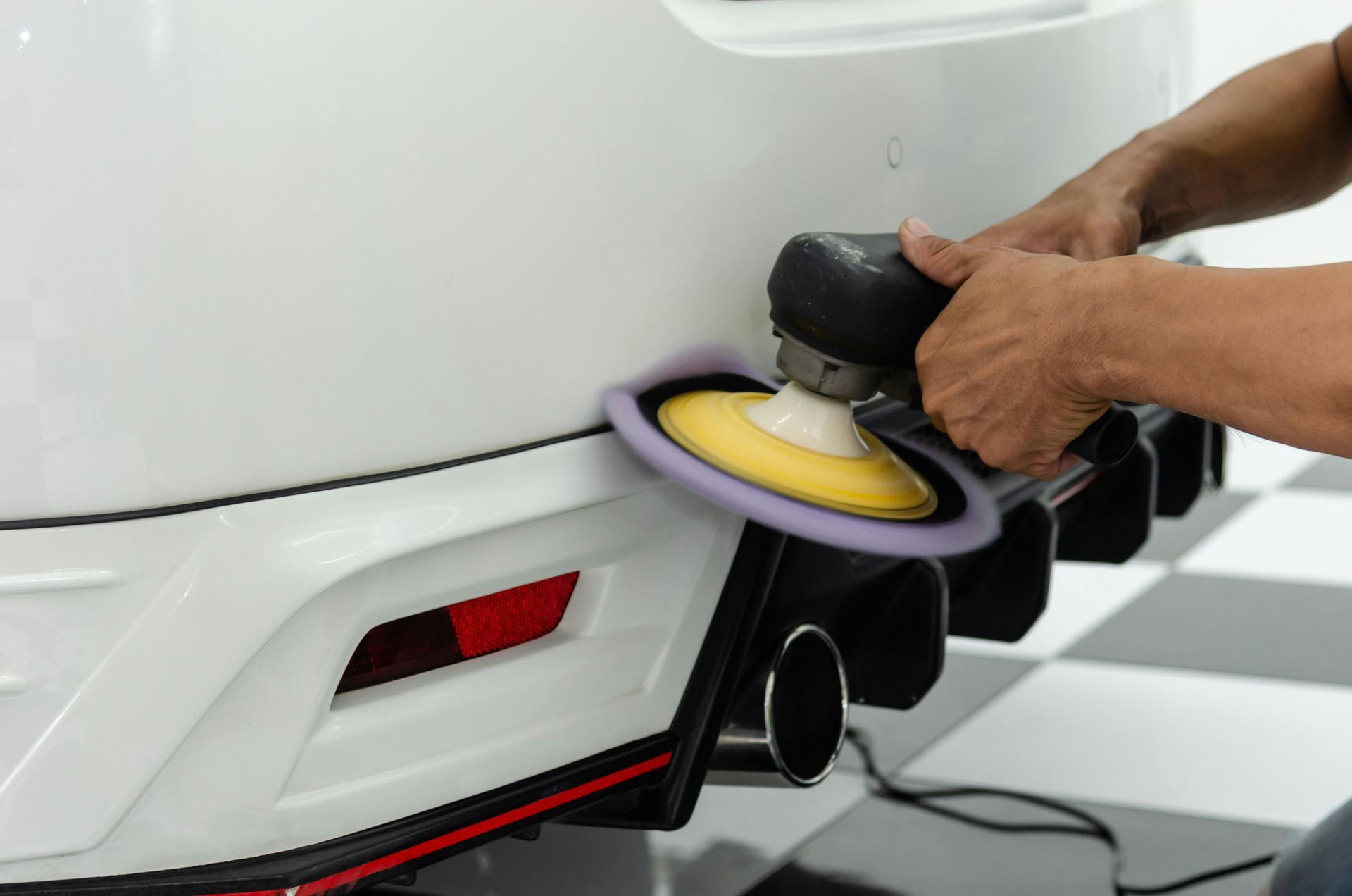 A man is polishing a white car with a machine.