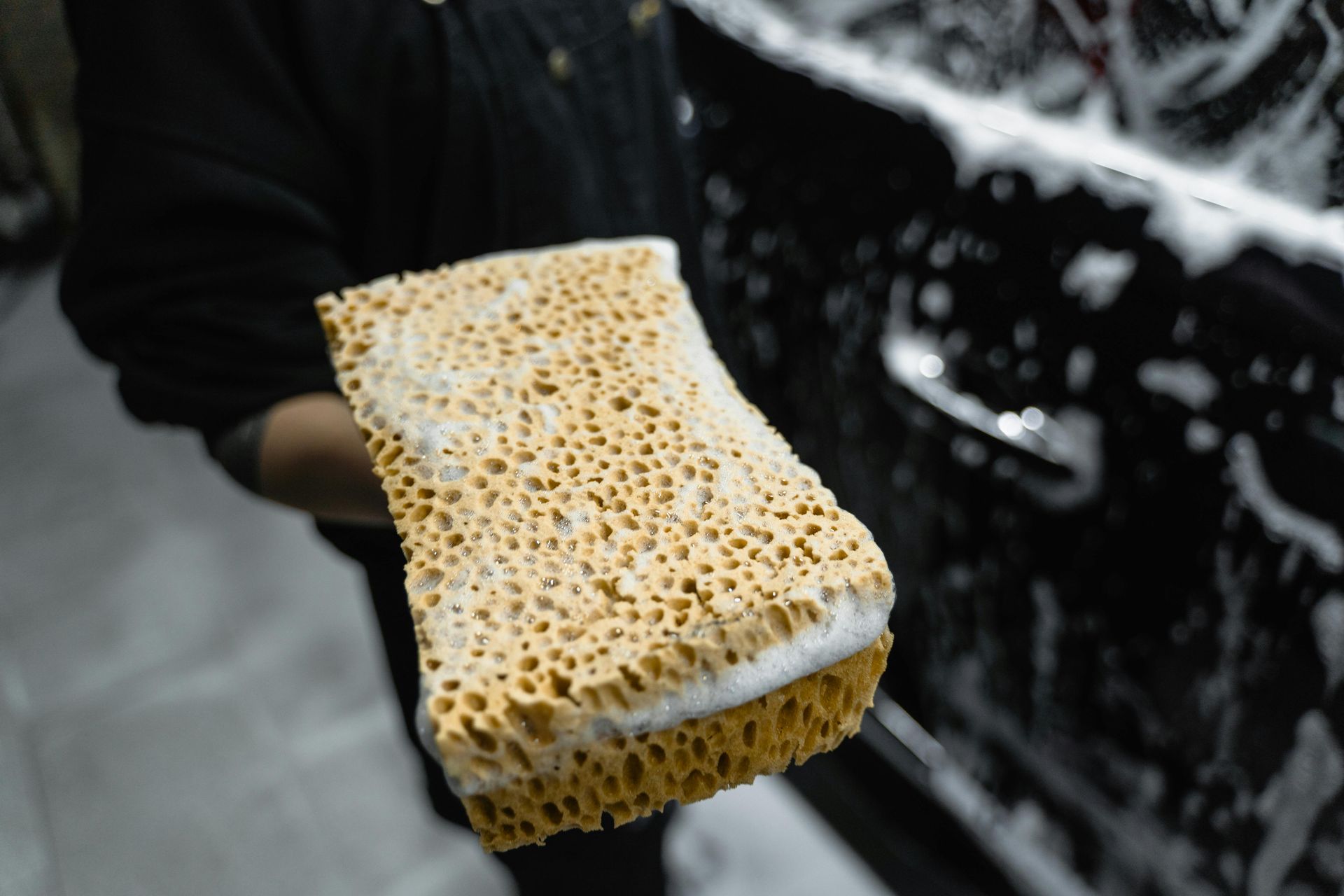 A person is holding a sponge in front of a car.